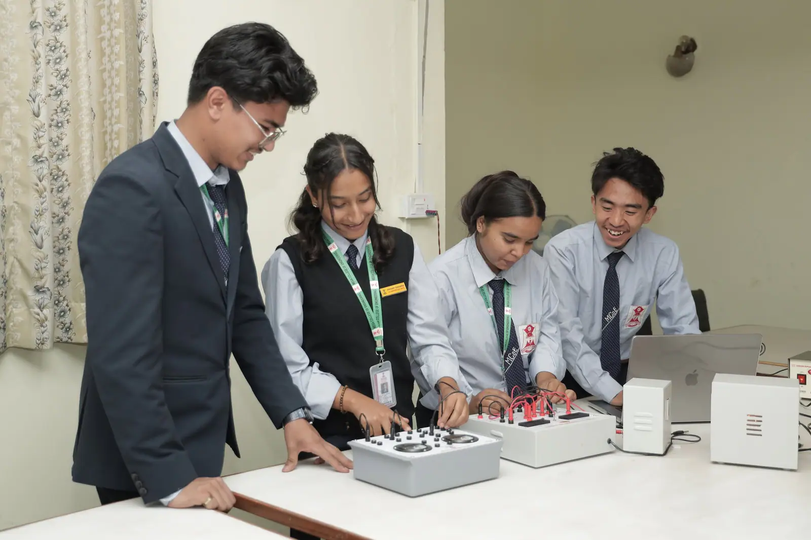 Four students round a bench of electronics trainer boards, one of them wiring a circuit