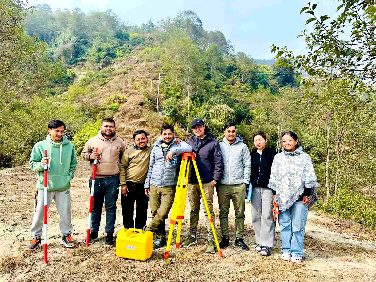 Eleven students round two survey tripods on a hillside, an instrument case open on the grass