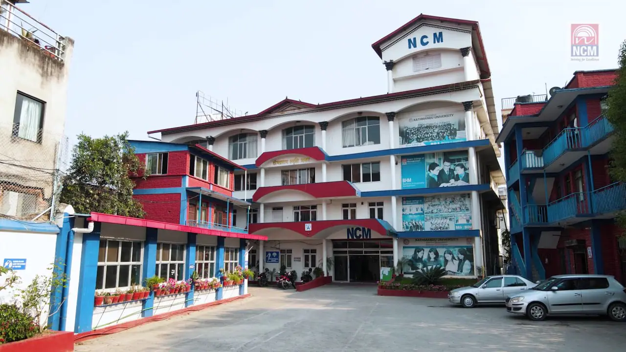 The blue and white college building with its NCM lettering above a paved forecourt