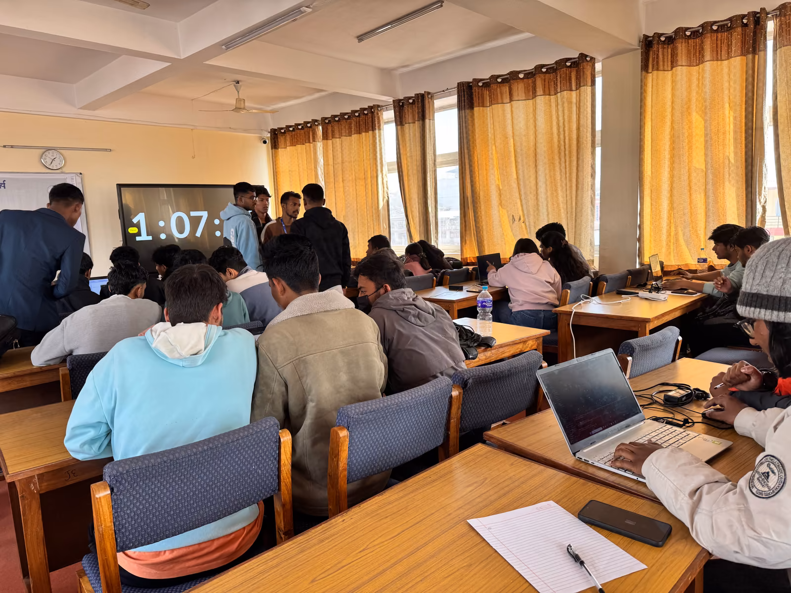 Students at laptops round tables with a countdown clock on the screen behind